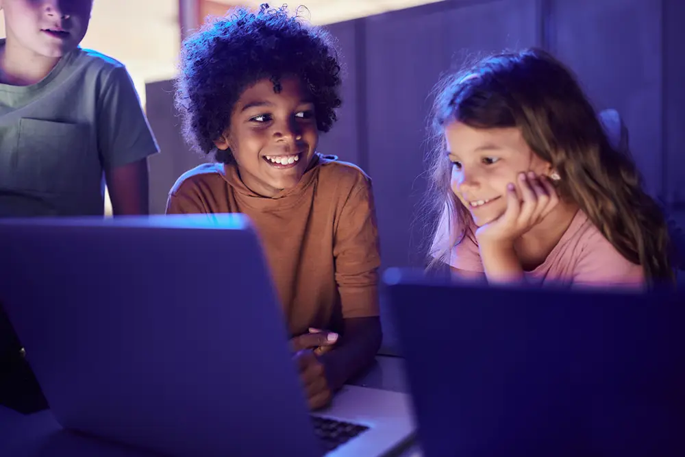 Children smiling together while using laptops